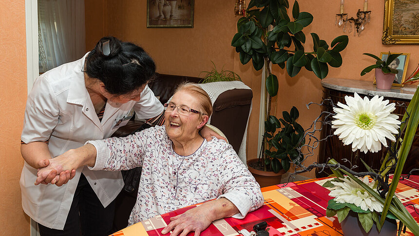 Exercice de mobilité avec une aide à domicile Filieris chez une dame âgée souriante