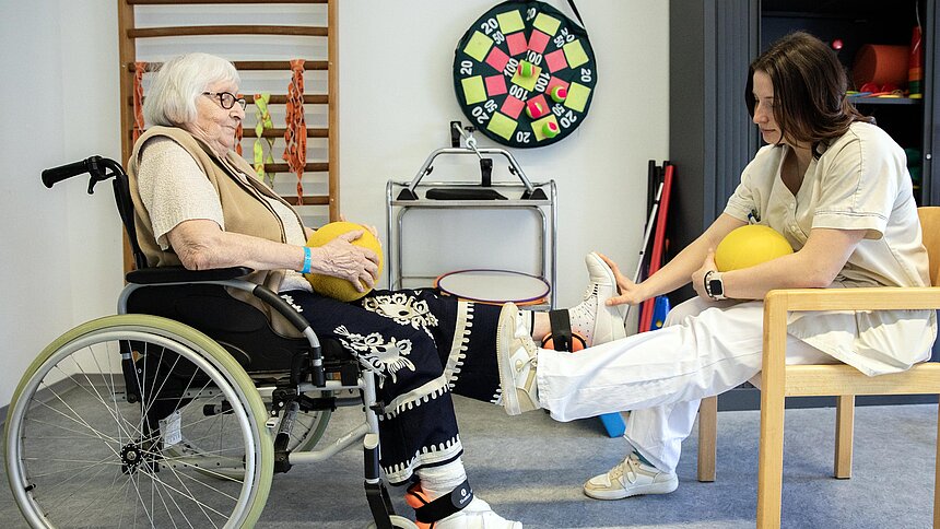Une patiente en fauteuil roulant s'exerce au niveau du pied avec la kinésithérapeute.