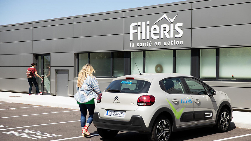 Une patiente entre dans le centre de santé. Une voiture Filieris est garée devant.