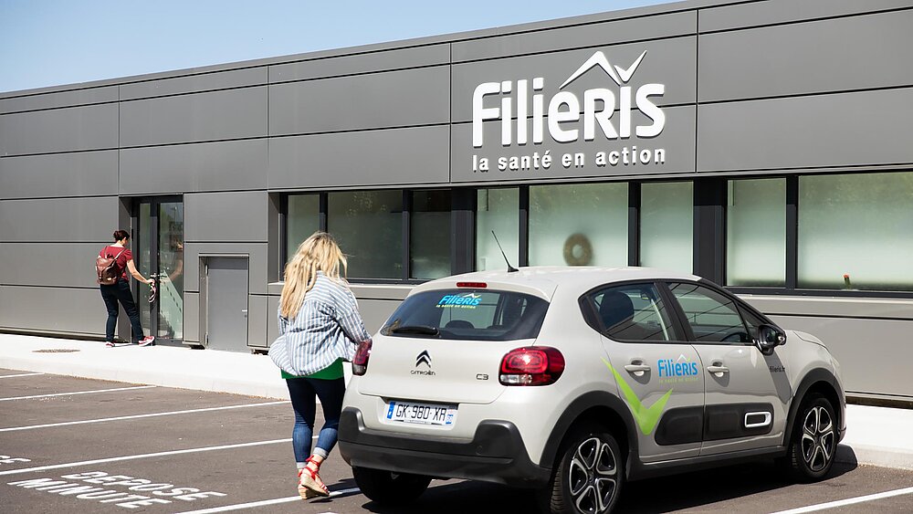 Une patiente entre dans le centre de santé. Une voiture Filieris est garée devant.