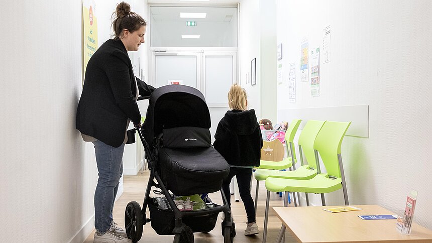 Une maman avec une poussette et un enfant patientent dans la salle d'attente.