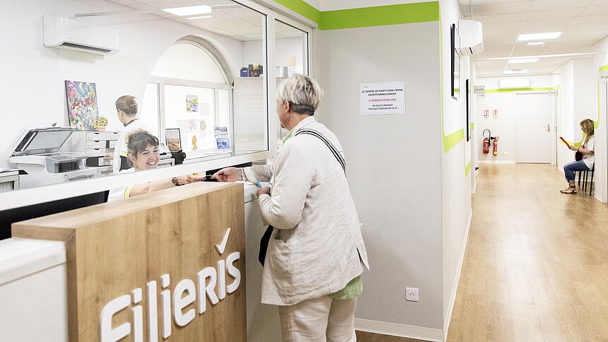 La secrétaire médicale reçoit une patiente au guichet d'accueil.