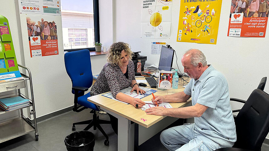 Une infirmière reçoit à son bureau un patient d'une soixantaine d'années.