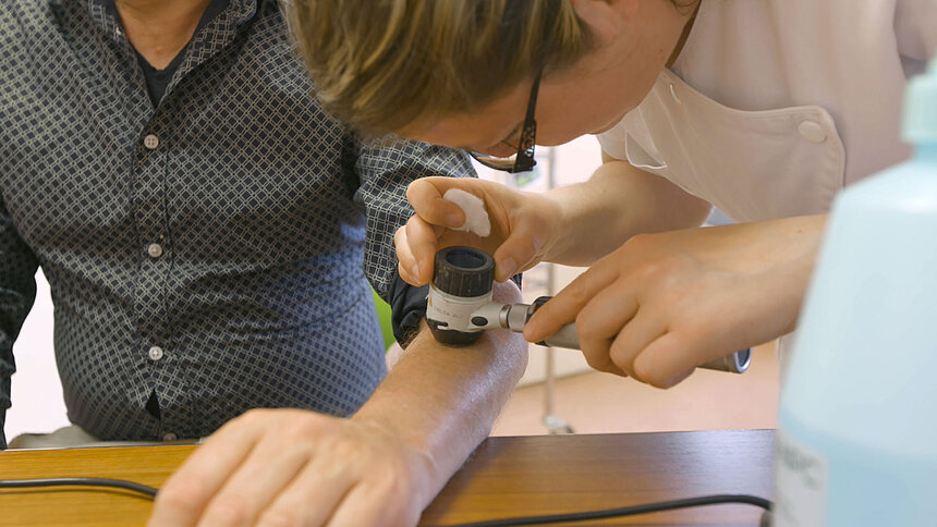 Une dermatologue examine un grain de beauté sur le bras gauche d'un patient.