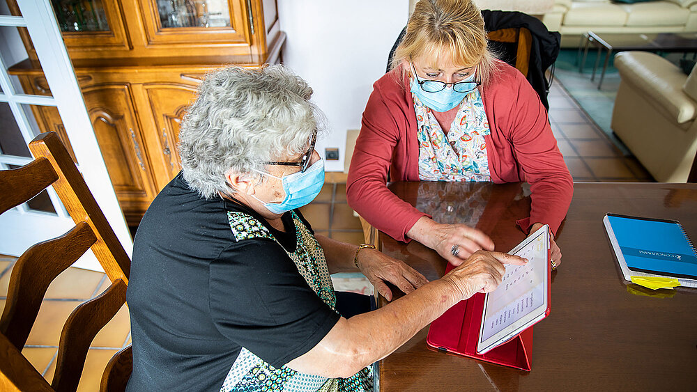 Une personne âgée se sert d'une tablette tactile avec le soutien d'une aide à domicile.