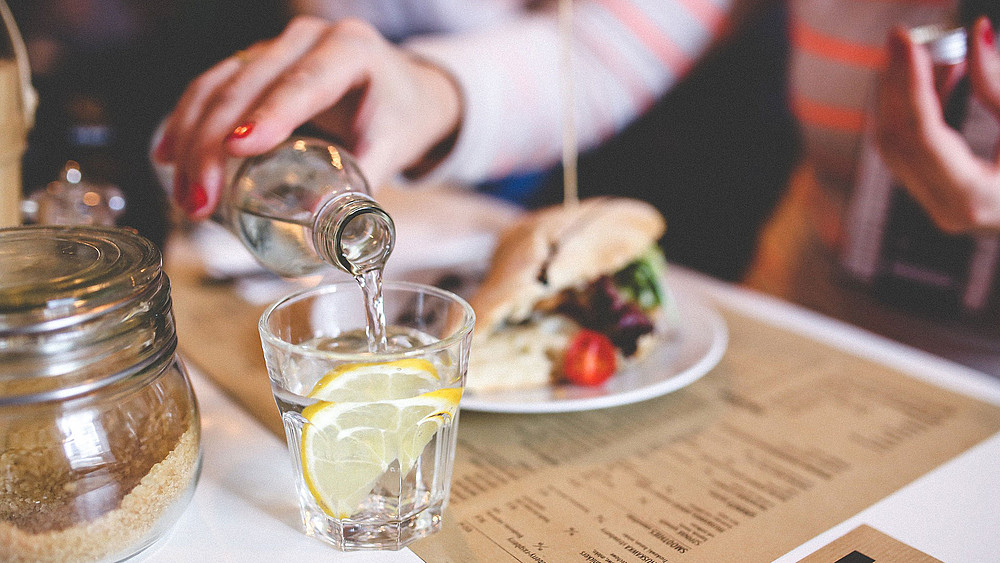 Gros plan sur la main d'une femme au restaurant qui verse de l'eau dans un verre avec un citron