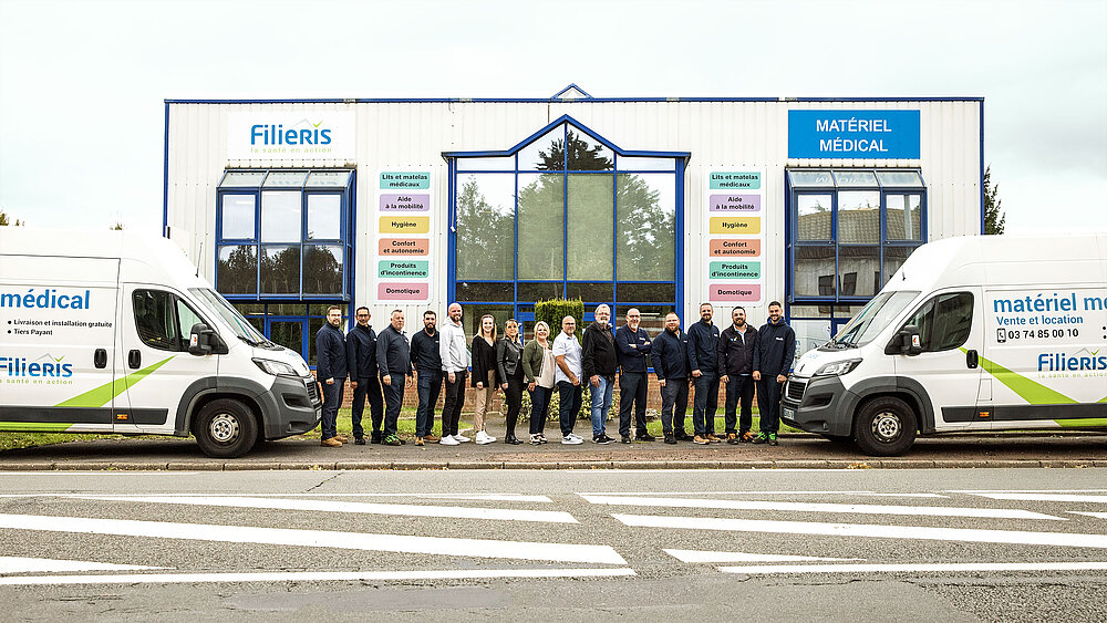 Les quinze femmes et hommes de l'équipe du matériel médical Filieris prennent la pose devant le bâtiment, encadrés par deux camions du service.