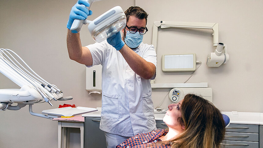 Un dentiste ausculte sa patiente allongée sur le fauteuil dentaire.