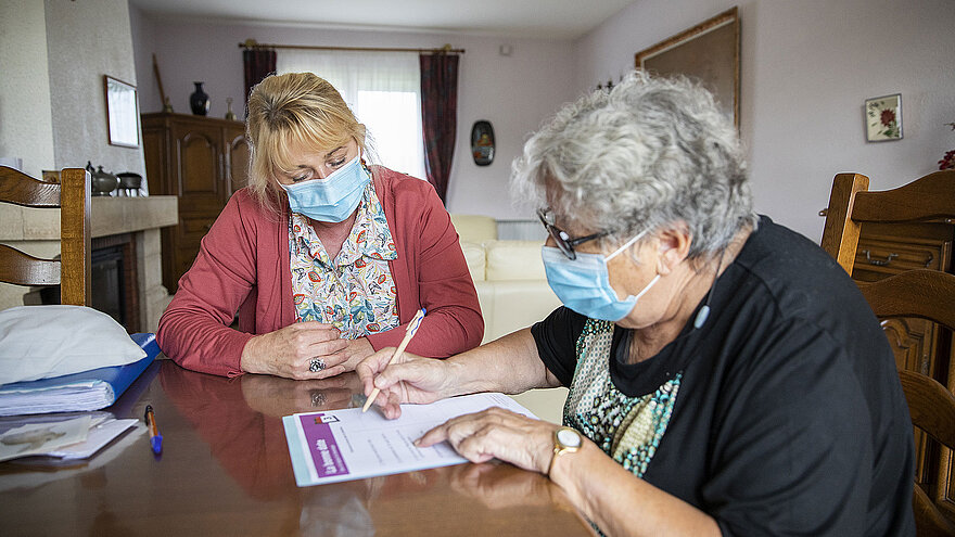 Une personne âgée signe des documents en présence de l'aide à domicile.