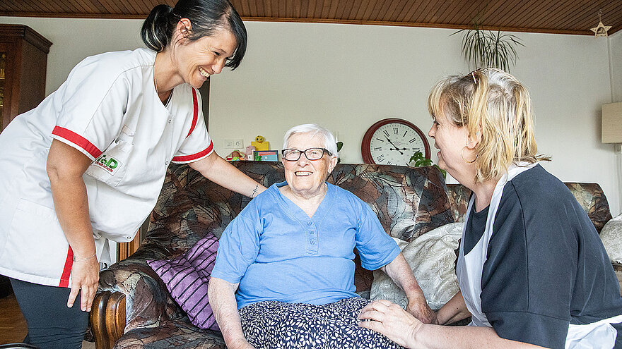 Une dame âgée entourée de ses deux aides à domicile