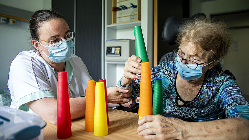 Une patiente empile des cônes en plastique sous le regard de l'ergothérapeute.