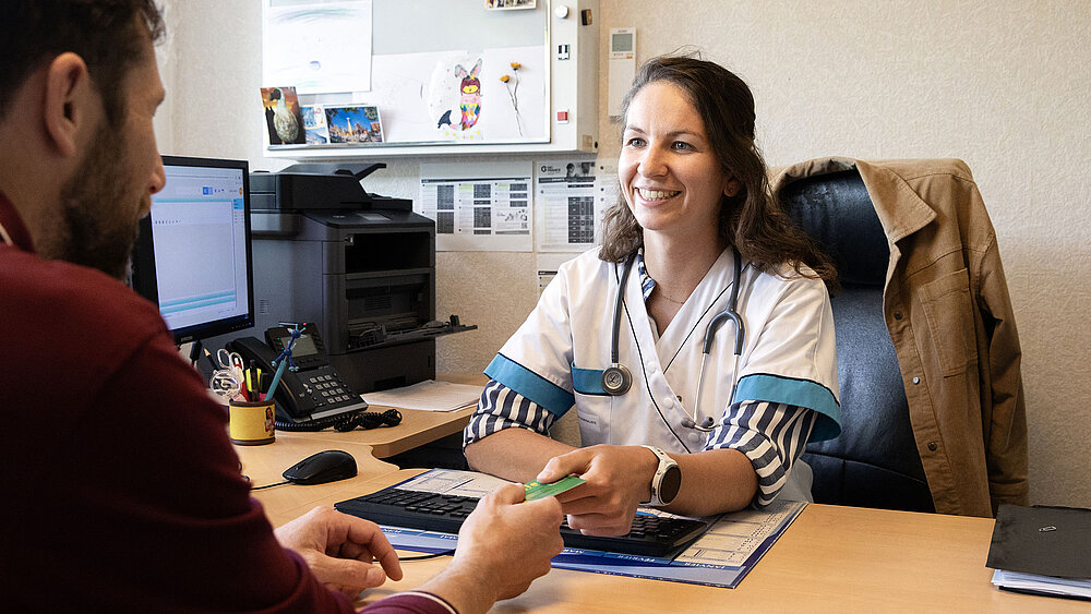 Une femme médecin prend la carte Vitale de son patient.